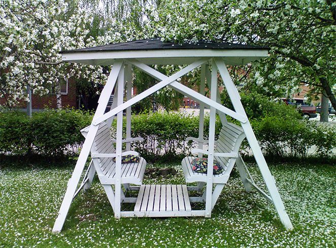 Vit herrgårdsgunga med tak bland blommande träd