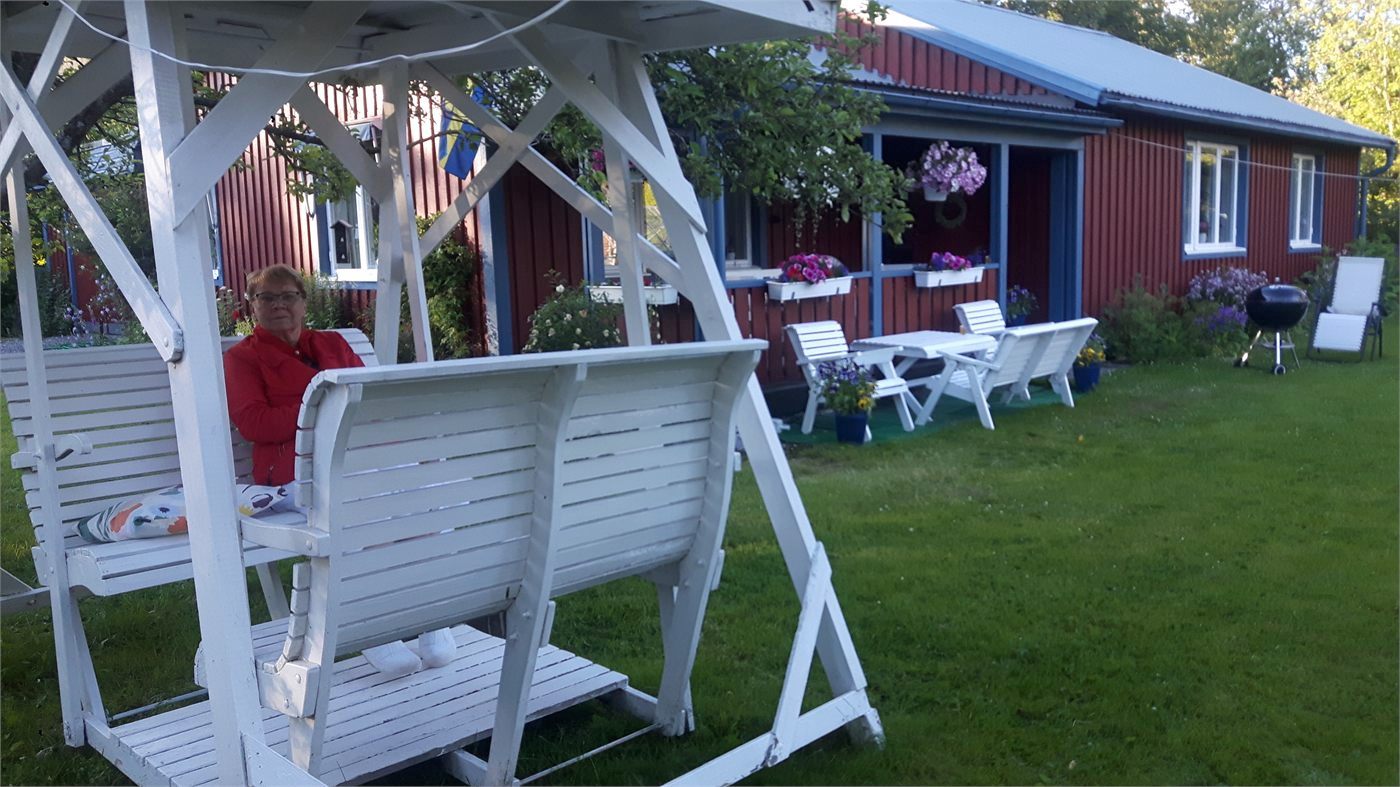 Vit gunga och sittgrupp vid ett rött hus under en sommarkväll